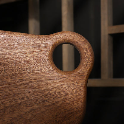Artistic irregular shaped ebony wood cutting board on a kitchen counter.